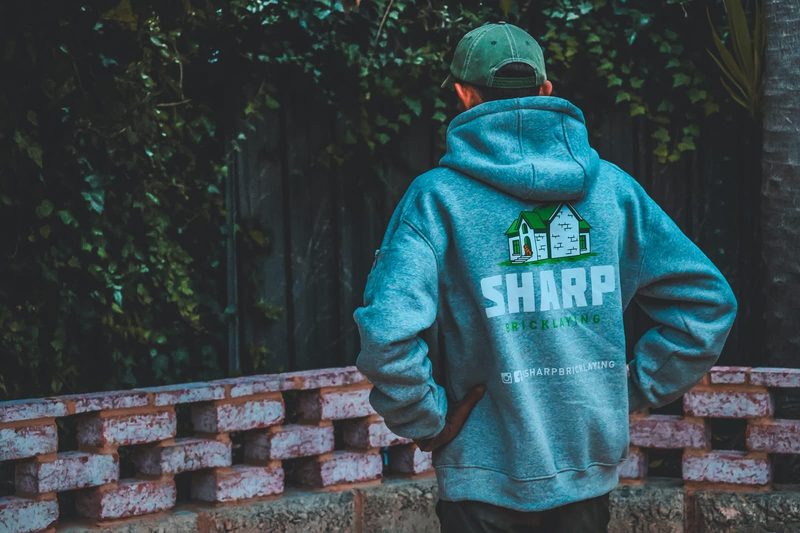 Crew member in a Sharp Bricklaying hoodie and cap, seen from behind